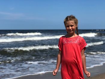 Smiling girl standing on shore at beach against sky during sunny day