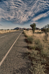 Empty road amidst field against sky