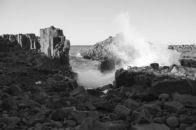 Waves splashing on rocks at shore against sky