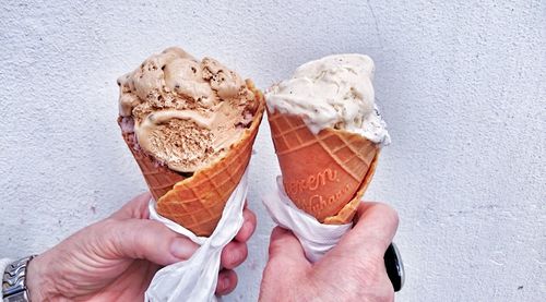 Close-up of hands holding ice cream cones against wall