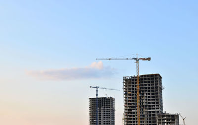 Low angle view of crane by building against sky