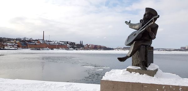 Statue by frozen lake against sky during winter