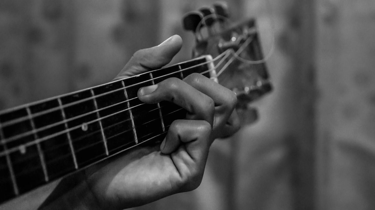 CLOSE-UP OF HANDS PLAYING GUITAR AGAINST BLURRED BACKGROUND