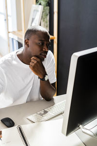 Male freelancer sitting with hand on chin looking at desktop computer in studio