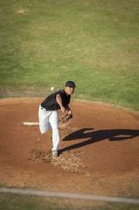 Teen baseball player in black and white uniform pitching