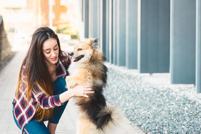 Woman playing with dog on footpath