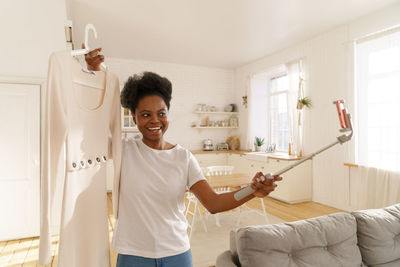 Smiling woman holding dress while talking on video call at home