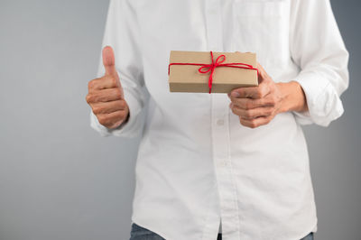 Midsection of man holding paper while standing against white background