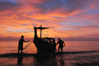 Silhouette men fishing on beach against sky during sunset