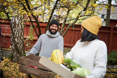 Smiling man and woman talking while holding freshly produce vegetable basket in yard