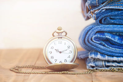 Close-up of pocket watch by stacked jeans on table