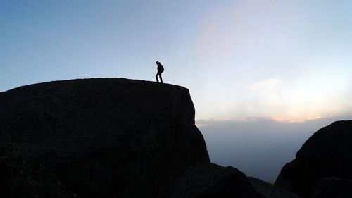 Silhouette man standing on rock against sky