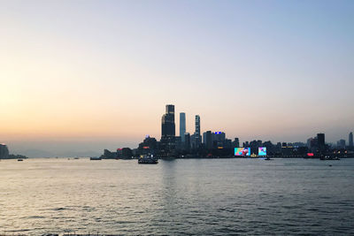 Sea by buildings against clear sky during sunset in hong kong