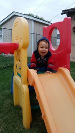 Cute cheerful kid sitting on plastic slide at back yard