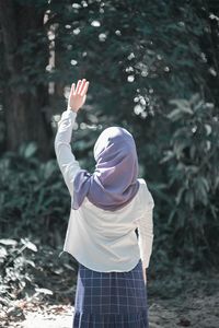 Rear view of woman with arms raised standing outdoors