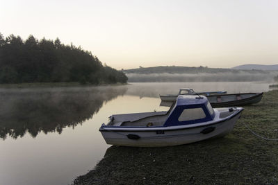 Boats moored beside misty lake at dawn