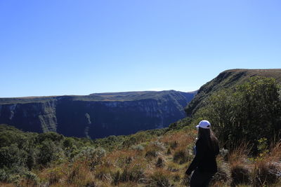 Rear view of man standing on mountain against clear blue sky