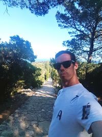 Man wearing sunglasses and trees against sky