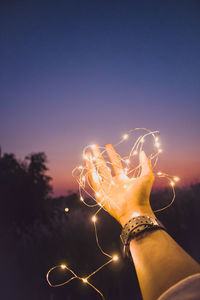 Person holding illuminated fireworks against sky at night