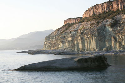 Rock formations by sea against clear sky