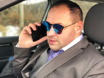 Businessman in sunglasses talking on mobile phone while sitting in car