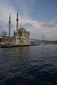 Tower bridge over sea against cloudy sky