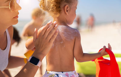 Close-up of mother applying sunscreen on daughter back