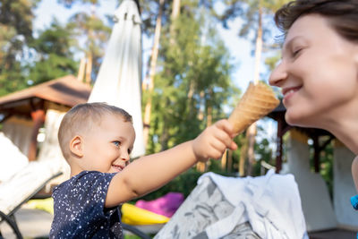 Cute boy feeding ice cream cone to mother outdoors