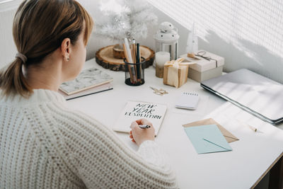 2022 goals, new year resolution. woman in white sweater writing text new year resolution in open