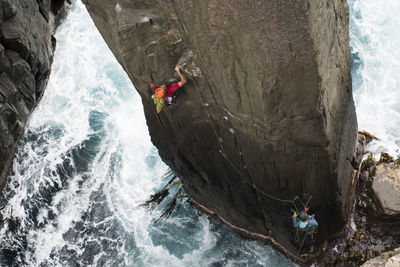 Rock climber grabs a crimp as he climbs a rock pilar out of the ocean in the totem pole, cape hauy, tasman national park, tasmania, australia.