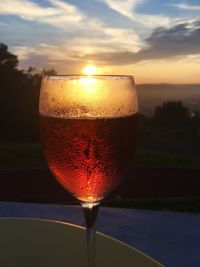 Close-up of beer glass against sunset sky