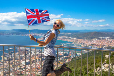 Portrait of smiling woman holding british flag while standing against cityscape