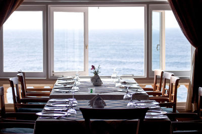 Chairs and tables in restaurant by sea seen through window