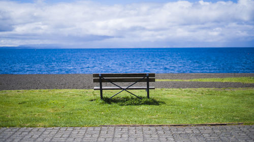 Empty bench by sea against sky