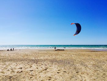 Person flying over sea against clear blue sky