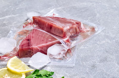 Red tuna fillets in vacuum package on gray marble background. fresh fish, lemon and parsley. 