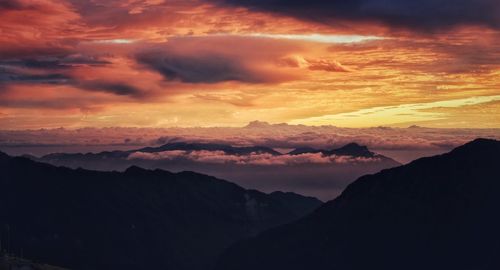 Scenic view of dramatic sky over silhouette mountains during sunset