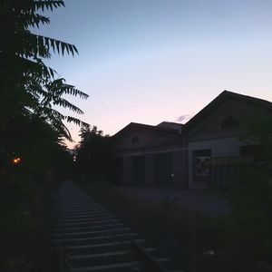 Street amidst houses and silhouette trees against sky at sunset