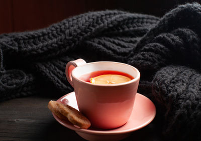 Pink cup of pomegranate tea and knitted scarf on black wooden background