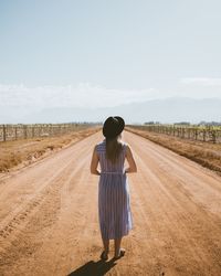 Rear view of woman standing on dirt road