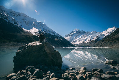 One man sitting on rock near the lake with snowcapped mountains reflection