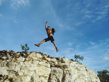 Low angle view of man jumping on rock against sky