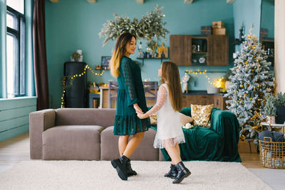 Mother and daughter holding hands in the living room of the house, decorated for christmas