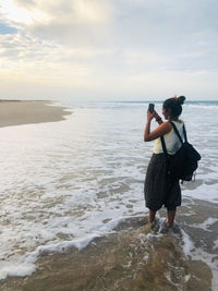 Girl photographing at beach against sky
