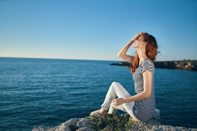 Woman sitting by sea against clear sky