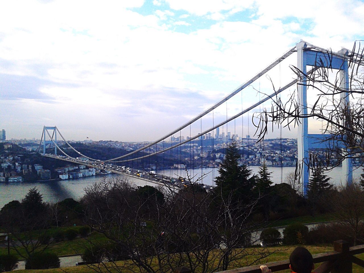 sky, bridge - man made structure, built structure, connection, architecture, cloud - sky, transportation, engineering, cloud, tree, cloudy, river, suspension bridge, outdoors, metal, day, low angle view, nature, city, no people