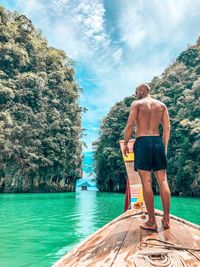 Rear view of shirtless man standing by sea against sky