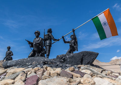 Low angle view of statues on rock against blue sky