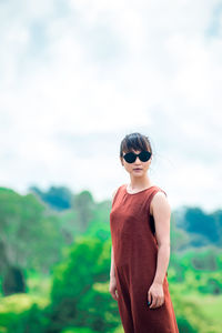 Young woman wearing sunglasses standing on mountain against cloudy sky