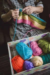 Box of different balls of wool and knitting senior woman